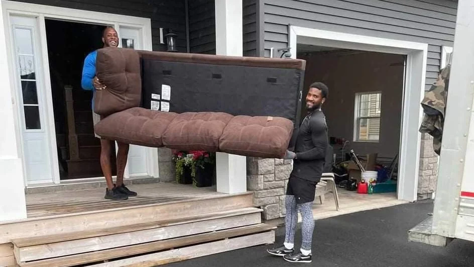 Two smiling movers carrying a couch out of a house