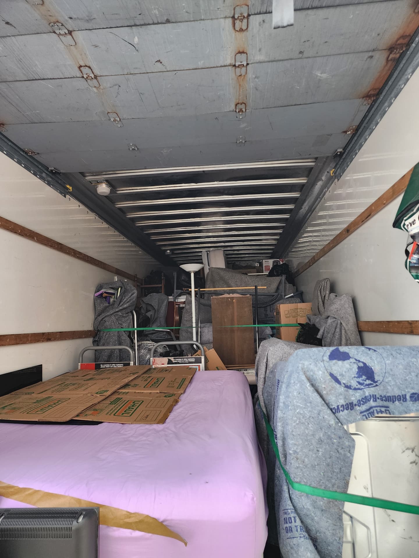 The inside of a moving truck, fully loaded with blanket-wrapped furniture strapped in place